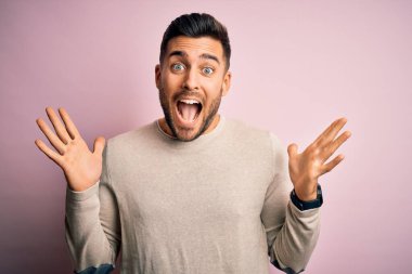 Soyutlanmış pembe arka planda dikilmiş, kollarını kaldırıp heyecanla haykırarak başarıyı kutlayan genç ve yakışıklı bir adam. Kazanan konsept