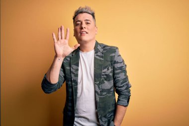 Sarı arka planda duran iş ceketi giyen yakışıklı ve modern bir adam beş numaralı parmaklarıyla gülümseyerek kendinden emin ve mutlu bir şekilde onu işaret ediyor..