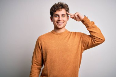 Sarışın, kıvırcık saçlı, beyaz arka planda sıradan bir süveter giyen tek parmağıyla gülümseyen, harika bir fikir ya da düşünce, iyi bir hafıza.