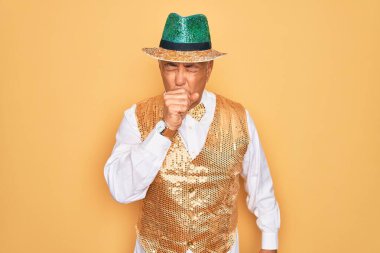 Sarı arka plan üzerinde Brezilya karnavalı kıyafeti giyen orta yaşlı, kır saçlı bir adam kendini iyi hissetmiyor ve soğuk algınlığı veya bronşitin belirtisi olarak öksürüyor. Sağlık hizmeti kavramı.