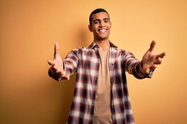 Sarı arka planda sıradan bir tişört giyen genç ve yakışıklı Afro-Amerikan adam kameraya sarılıp gülümsüyor. Mutluluğu kucaklayan neşeli bir ifade..