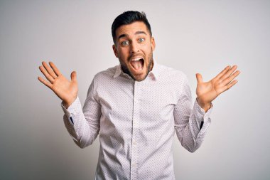 Zarif gömlekli genç adam, izole edilmiş beyaz arka planda duruyor çılgın ve başarıyı kollarını kaldırıp heyecanla haykırarak kutluyor. Kazanan konsept