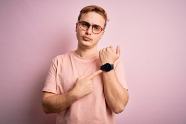 İzole edilmiş pembe arka plan üzerinde duran sıradan tişörtlü genç ve yakışıklı bir adam. Aceleyle saati, sabırsızlığı ve rahatlamış bir ifadeyle kameraya bakıyor.