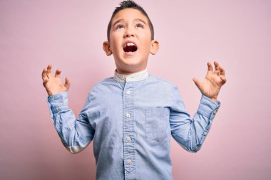 Zarif bir gömlek giyen küçük çocuk pembe izole edilmiş arka plan üzerinde duruyor çılgın ve kızgın bir şekilde bağırıyor ve agresif bir ifade ve kollarla bağırıyor. Hayal kırıklığı konsepti.