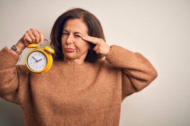 Orta yaşlı esmer kadın, izole edilmiş arka planda klasik çalar saati tutuyor. Birini vuruyor ve öldürüyor. Silah gibi el ve parmaklarını işaret ediyor..