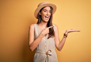 Genç, güzel, esmer kadın tatilde. Sıradan bir elbise giyiyor ve şapkasını takmış. Kameraya hayret ediyor ve gülümsüyor..