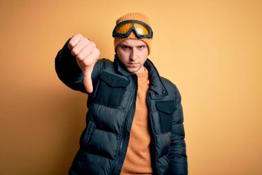 Kış için şapka, palto ve kayak gözlüğü takan yakışıklı beyaz bir adam mutsuz ve kızgın görünüyor. Reddedildiğini gösteriyor. Kötü ifade.