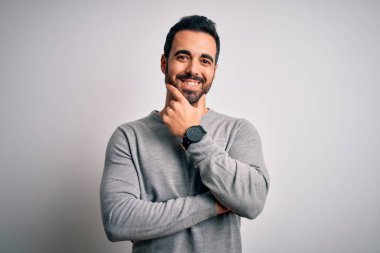 Sakallı, sıradan bir süveter giyen, beyaz arka plan üzerinde duran, kolları çapraz ve çenesi havada kameraya gülümseyen genç yakışıklı bir adam. Olumlu düşünüyorum..