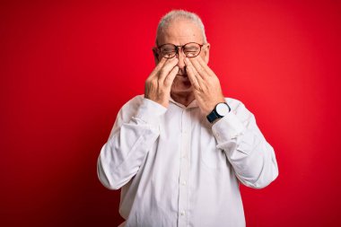 Orta yaşlı yakışıklı, beyaz gömlekli, kırmızı arka planda gözlüklü, yorgun, uykulu ve yorgun bir adam. Görüş sorunu