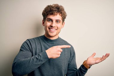 Sarışın, kıvırcık saçlı, beyaz arka planda sıradan bir süveter giyen genç adam kameraya hayret ediyor ve gülümsüyordu..