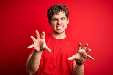 Sarışın, kıvırcık saçlı, kırmızı arka planda sıradan tişörtler giyen komik bir şekilde kedi gibi pençe hareketi yapan, agresif ve seksi bir ifade sergileyen genç, yakışıklı bir adam.