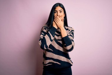 Pembe arka planda hayvan desenli süveter giyen genç ve güzel bir İspanyol kadın yanlışlıkla elleriyle ağzını kapatmış. Gizli konsept.