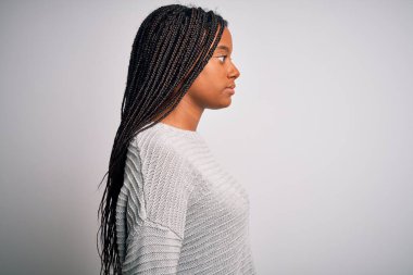 Genç Afro-Amerikalı kadın, gri izole bir arka plan üzerinde rahat ve rahat duruyor. Yan tarafa bakıyor, rahat poz veriyor, kendine güvenen bir gülümsemeyle doğal bir poz veriyor..