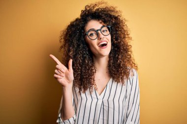 Kıvırcık saçlı, piercingli, çizgili gömlekli ve gözlüklü genç ve güzel bir kadın başarılı bir fikri işaret ediyor. Heyecanlı ve mutlu. Bir numara..