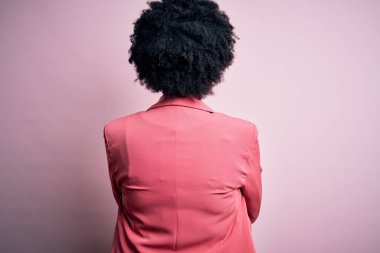 Kıvırcık saçlı, pembe ceketli, kollarını kavuşturup arkasını çeviren Afro-Amerikalı genç, güzel bir iş kadını.