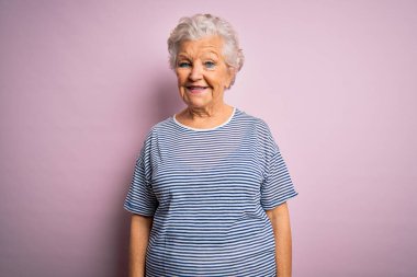 Son sınıftaki güzel gri saçlı kadın pembe arka planda rahat bir tişört giyiyor ve yüzünde mutlu ve havalı bir gülümseme var. Şanslı kişi..