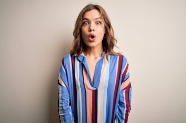 Renkli çizgili gömlek giyen genç sarışın kız izole edilmiş arka planda korkmuş ve şaşkınlık dolu bir ifade, korku ve heyecanlı bir yüz ifadesiyle şoka uğramış..