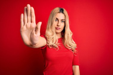 İzole edilmiş kırmızı arka planda duran ve avucunun içi gibi şarkı söylemeyi kesen gündelik tişört giyen genç, güzel sarışın kadın. Yüzünde olumsuz ve ciddi bir jest olan uyarı ifadesi.
