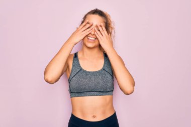 Genç, sarışın, mavi gözlü sporcu kadın spor kıyafetleri giyip gözleri kapayarak neşeli ve komik bir şekilde gülümsüyor. Kör kavram.