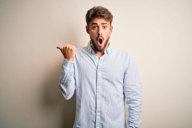 Beyaz arka planda duran çizgili tişörtlü, sakallı, yakışıklı genç bir adam..