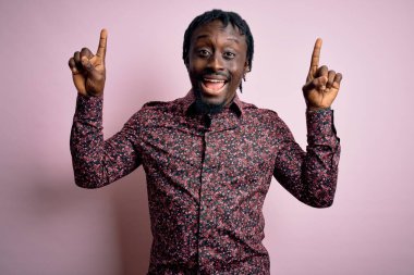 Genç, yakışıklı, Afro-Amerikalı bir adam pembe arka planda dikilmiş şaşkın şaşkın, parmaklarıyla işaret ediyor ve kollarını kaldırıyordu..
