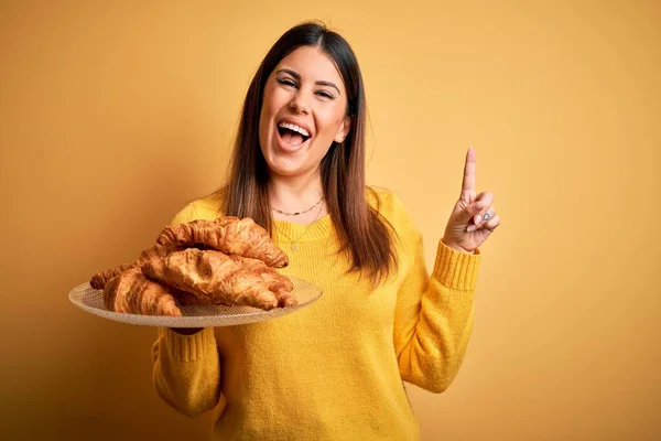 Young Beautiful Woman Holding French Croissant Pastry Yellow Background Surprised — Stock Photo, Image