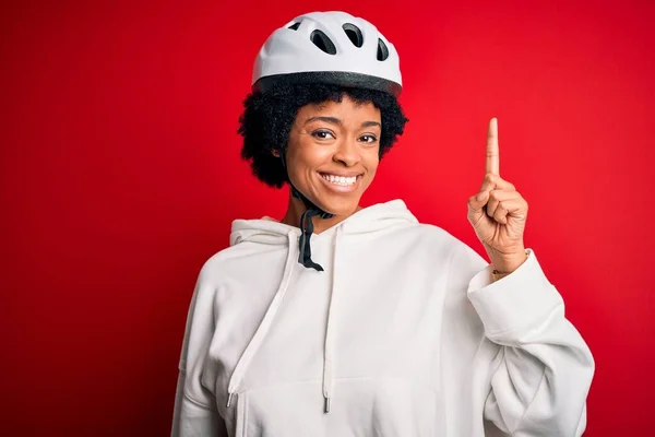 若いアフリカ系アメリカ人のアフロサイクリングの女性が成功したアイデアで指を指して自転車のセキュリティヘルメットを着て巻き毛を持つ 興奮し 第一番 — ストック写真