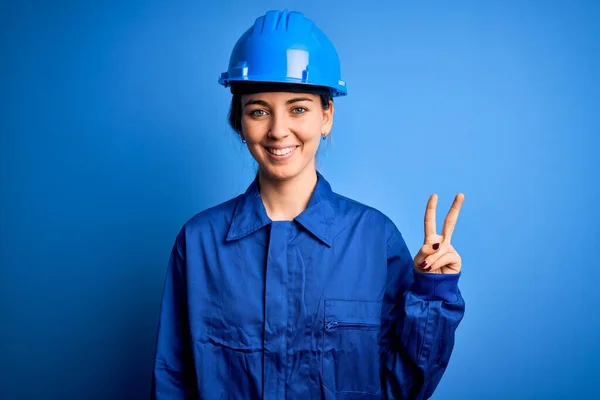 青い目の若い美しい労働者の女性は セキュリティヘルメットを着用し 勝利のサインを行うカメラでの幸せな顔のウィンクで一様な笑顔 第二番 — ストック写真