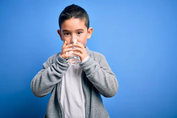 可爱的幼儿 喝着一杯健康的水 站在孤立的蓝色背景之上 — 图库照片