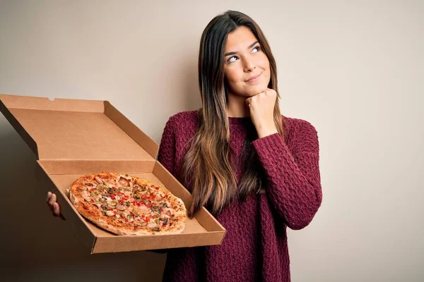 年轻美丽的姑娘拿着意大利披萨的送货盒站在白色的背景下严肃地思考着问题 非常迷惑的想法 — 图库照片