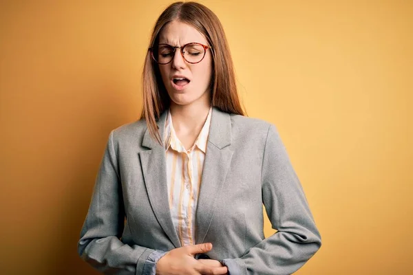 若い美しい赤毛の女性のため 吐き気 痛みを伴う病気の気分が悪く胃の手で孤立した黄色の背景にジャケットや眼鏡を着用 アチェの概念 — ストック写真