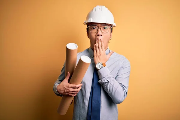 年轻英俊的中国建筑师 戴着眼镜 头戴安全帽 手持设计图 双手捂住嘴 为错误 神秘的表情而感到羞愧 — 图库照片