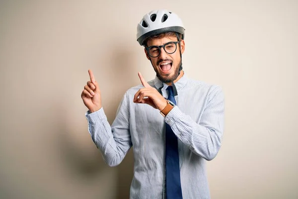Young businessman wearing glasses and bike helmet standing over isolated white bakground smiling and looking at the camera pointing with two hands and fingers to the side.