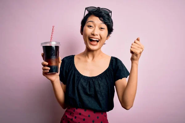 年轻美丽的中国女人喝可乐 用稻草盖着粉红的背景 喝着清澈的饮料 自豪地尖叫着 庆祝着胜利和成功 激动地欢呼着 — 图库照片
