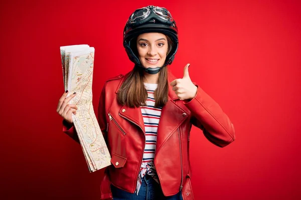若い美しい観光オートバイの女性は大きな笑顔で幸せな都市マップを保持するオートバイのヘルメットを身に着けていますOkのサインを行います 指で親指アップ 優れたサイン — ストック写真