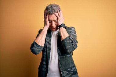 Sarı arka planda duran iş ceketi giyen yakışıklı, çaresiz ve stresli bir genç adam. Çünkü acı ve migren ağrısı var. Ellerini başının üstüne koy..