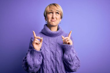 Kısa saçlı, balıkçı yaka kazak giyen, mor arka planda üzgün ve üzgün görünen mutsuz ve depresif yönünü gösteren genç sarışın kadın..