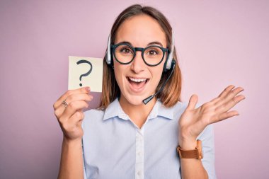 Güzel çağrı merkezi ajanı kadın elinde kulaklıkla çalışıyor. Soru işareti ile çok mutlu ve heyecanlı. Kazanan ifade zaferi kutluyor.