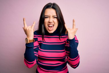 Pembe izole arka planda çizgili tişört giyen zarif, genç bir kadın çılgın bir ifadeyle elleri havada rock sembolü yaparak bağırıyor. Müzik yıldızı. Ağır konsept.