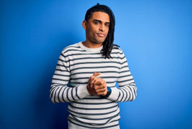 Rastgele çizgili süveter giyen, elleri çapraz parmaklı, gevşemiş ve neşeli gülümseyen Afro-Amerikan genç adam. Başarı ve iyimser