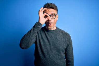 Mavi arka planda duran sıradan süveter ve gözlük takan genç yakışıklı adam şaşırmış yüz ifadesiyle şaşırmış, parmaklarından bakan gözler. İnançsız ifade.