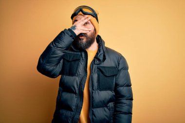 Sakallı, kar maskesi takmış, kar maskesi takmış, kar maskesi takmış yakışıklı kayakçı. Yüzü ve gözleri kapalı, utangaç bir ifadeyle parmaklarının arasından bakıyor..