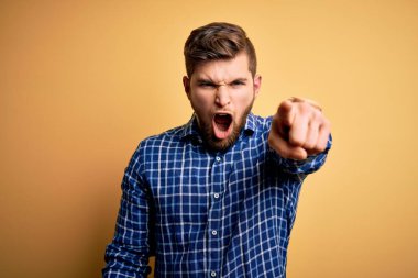 Sarışın, sakallı ve mavi gözlü genç bir işadamı sarı arka planda gömlek giyiyor. Kameraya kızgın ve sinirli olduğunu gösteriyor.