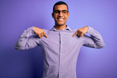 Yakışıklı Afro-Amerikalı adam mor arka planda çizgili gömlek ve gözlük takıyor. Yüzünde bir gülümsemeyle, gururlu ve mutlu bir şekilde kendini gösteriyor..