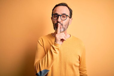 İzole edilmiş sarı arka planda günlük süveter ve gözlük takan orta yaşlı beyaz bir adam sessiz olmak istiyor. Sessizlik ve gizli konsept.