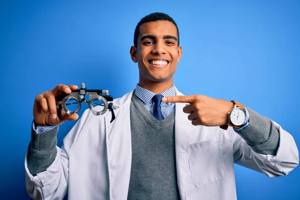 Yakışıklı afro-amerikan optik adam mavi arka planda optometri gözlüğü tutuyor.
