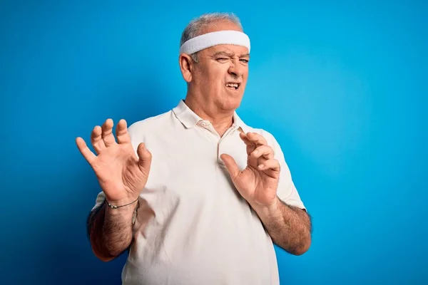 Middle age hoary sportsman doing sport wearing sportswear over isolated blue background disgusted expression, displeased and fearful doing disgust face because aversion reaction. With hands raised