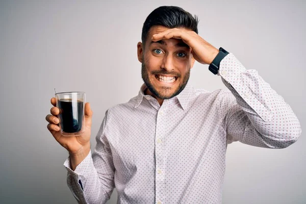 Young handsome man drinking a cup of hot coffee over white isolated background stressed with hand on head, shocked with shame and surprise face, angry and frustrated. Fear and upset for mistake.