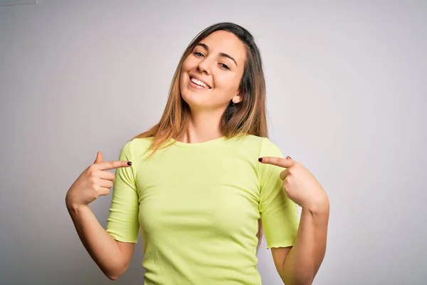 白い背景に緑色のカジュアルなTシャツを身に着けている青い目の美しいブロンドの女性は 顔に笑顔で自信を持って見て 誇りに思って幸せな指で自分自身を指して — ストック写真