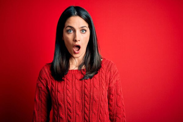 Young brunette woman with blue eyes wearing casual sweater over isolated red background afraid and shocked with surprise and amazed expression, fear and excited face.